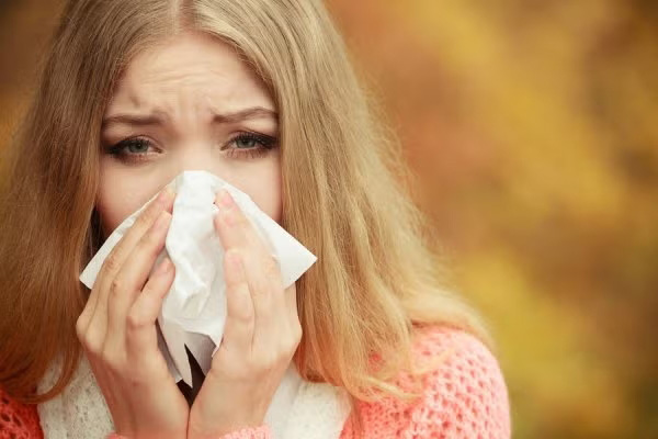 A woman with a tissue, blowing her nose