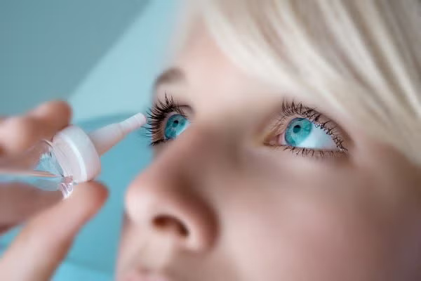 A woman applying eye drops to her right eye