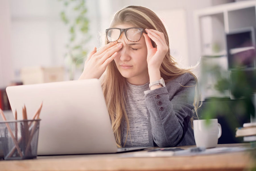 a woman working on laptop holding her eye in pain