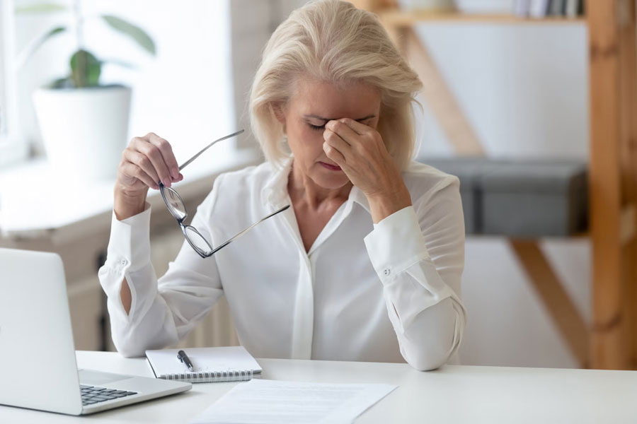 a woman working on laptop holding her eye in pain