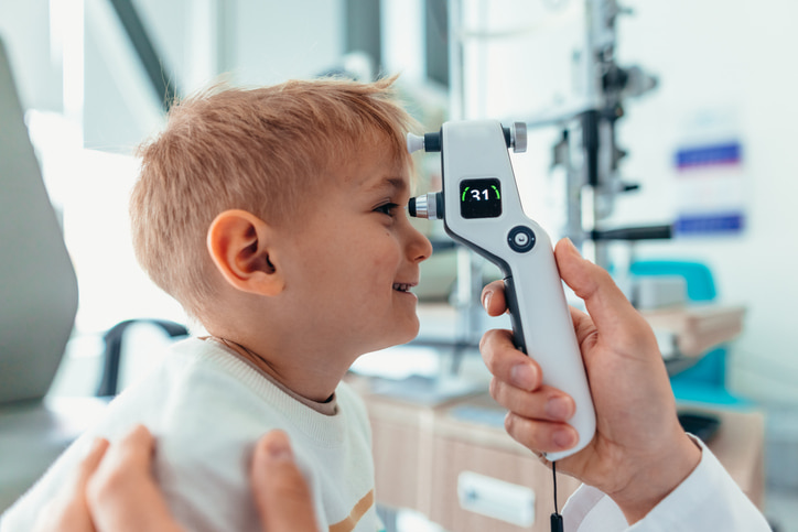 A child receiving an eye test with a handheld tonometer during a pediatric eye exam in Southern NH